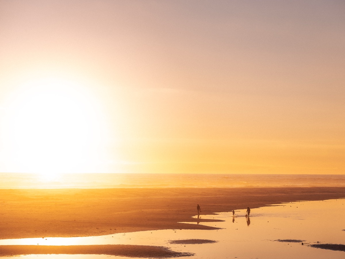 Silhouettes on a wide beach at golden hour, low sun reflecting off wet sand and tidal pools