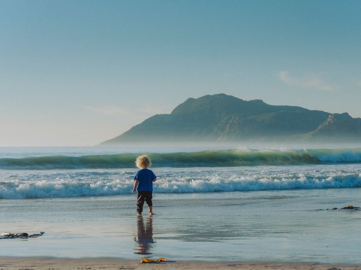 A child walking toward the ocean waves, mountain rising through haze in the distance